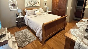 Une chambre avec un lit en bois, un ventilateur de plafond et une armoire en bois.