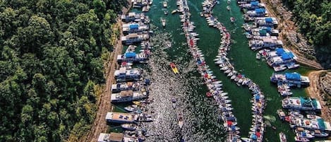 An aerial view of a river with numerous boats docked along the banks, surrounded by dense forest.