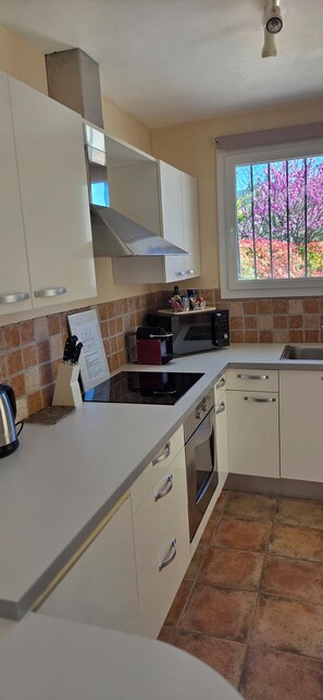 A modern kitchen with white cabinetry, a gas stove, a built-in oven, and a window with a view of flowers.