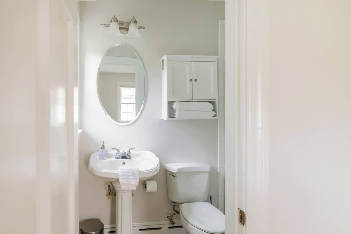 A bathroom with a pedestal sink, a toilet, a mirror, and a cabinet above the toilet.