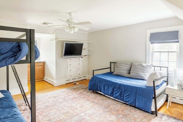 A bedroom with a bunk bed, a single bed, a ceiling fan, a TV, and a window with blinds.