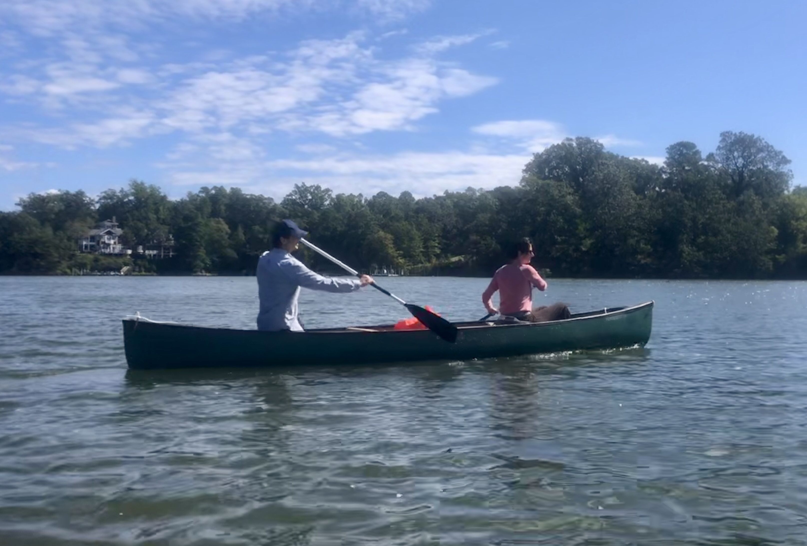 A canoe on calm water with a person paddling and another person sitting.