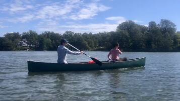 A canoe on calm water with a person paddling and another person sitting.