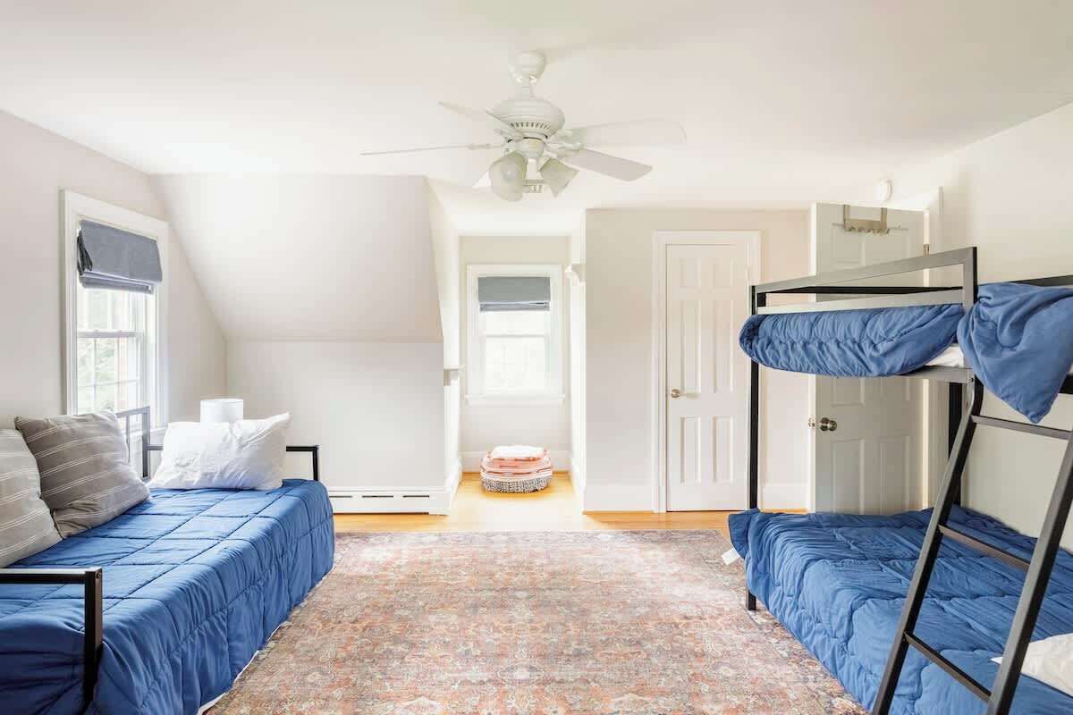 Een kamer met een stapelbed, een enkel bed en een plafondventilator.