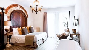 Un dormitorio con una cama grande, una bañera blanca, una silla colgante y un arco de ladrillo.