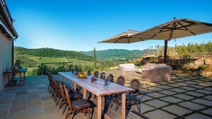 Un patio al aire libre con una mesa de comedor, sillas y un paraguas grande.