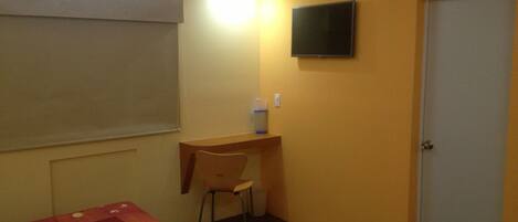 A small room with a bed, a desk, a chair, a television, and a door.