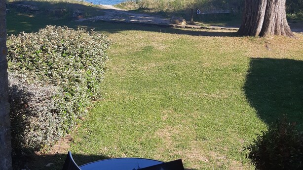An outdoor patio with a table and chairs, a large tree, and a view of the sea with boats. - T1 with sea view and access 30 meters (Sarzeau)