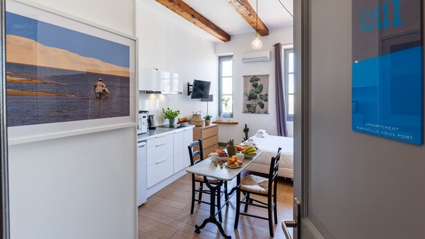 A modern kitchen with white cabinets, a dining table with chairs, and a hanging light fixture. - AZUR - LES COCONS - Studio Apartment, Sleeps 2 (Marseille)