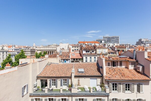 A cityscape with traditional terracotta-tiled rooftops, a mix of residential and commercial buildings, and a clear blue sky.