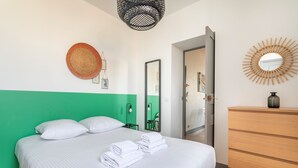 A neatly made bed with white linens and towels, a green accent wall, a wooden dresser, and a mirror with a bamboo frame. - JADE - LES COCONS - One Bedroom Apartment, Sleeps 2 (Marseille)