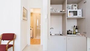 Cocina compacta con microondas, pileta y botella de vino. Se ve una silla roja en primer plano.