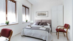 Un dormitorio ordenado con cama, dos sillas, una mesa y un armario.