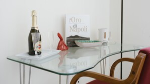 Una mesa de vidrio con una botella de Martini Rosé, un libro titulado 'L'Oro di Napoli' y un tazón de cerámica.