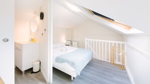 A bedroom with a bed, a white dresser, a mirror, and a skylight.