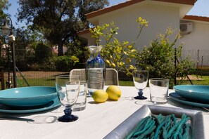 A table set outdoors with a white tablecloth, a blue vase, two lemons, and various glassware.