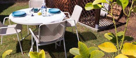 Mesa redonda con sillas, una botella y platos, todo dispuesto al aire libre.