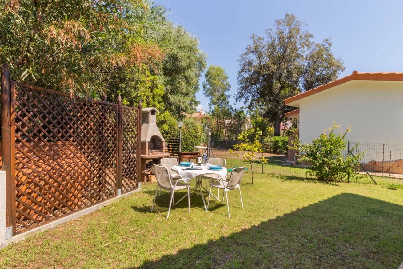 Een achtertuin met een barbecue, een tafel met stoelen en een kleine tuin.