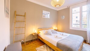 A bedroom with a wooden bed, bedside lamps, a ladder, a window with a view, and a hanging light fixture. - L'Imperti'Nantes- T3bis de Standing (Nantes)