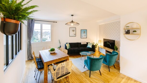 A modern living room with a dining table, sofa, and chairs, a TV, and a hanging plant. - L'Imperti'Nantes- T3bis de Standing (Nantes)