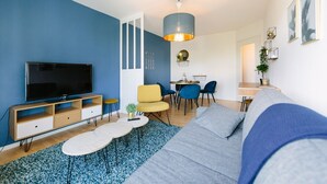 Ein modernes Wohnzimmer mit Fernseher, einer Couch, Sesseln und einem Essbereich.
