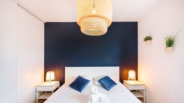 Ein modernes Hotelzimmer mit einem großen Bett, zwei Nachttischen mit Lampen, einer Wand in dunkler Farbe und kleinen Blumentöpfen.