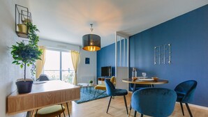 Ein modernes Wohnzimmer mit einem Holzesstisch, blauen Stühlen, einem Topfpflanzen, einer Hängelampe und einem großen Fenster mit Vorhängen.
