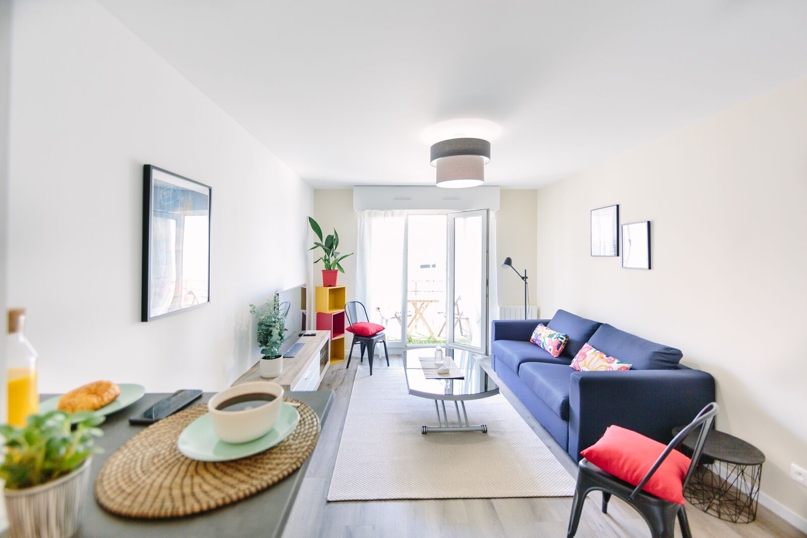 Una sala de estar moderna con un sofá azul, una mesa de centro y un comedor con una planta y una botella de jugo de naranja.