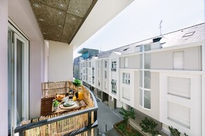 A balcony with a breakfast setup, including a table with bread, a plant, and a bottle of orange juice.