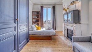 A bedroom with a bed, a fireplace, a sofa, a bookshelf, and a view through a window. - LE VICTOR - Grand et lumineux T3 (Bordeaux)