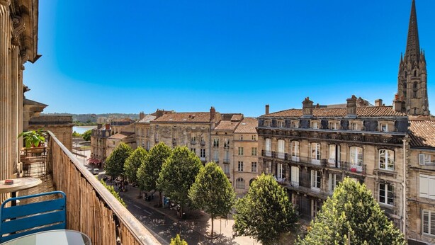 A balcony with a view of a city street, historic buildings, and a church spire. - LE VICTOR - Grand et lumineux T3 (Bordeaux)
