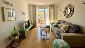 A living room with a sofa, a TV, a small table, and a decorative mirror. - Apartamento Jardines PG004 - Benitachell, Costa Blanca (Benitachell)