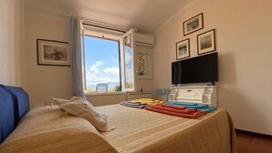 A hotel room with a bed, a TV, a window with a view, and a radiator. - The house in the carob trees with breathtaking views (Arcola)