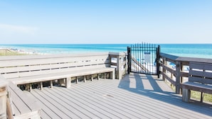 Ein hölzerner Steg führt zu einem Strand, an dem ein Tor und Bänke stehen.