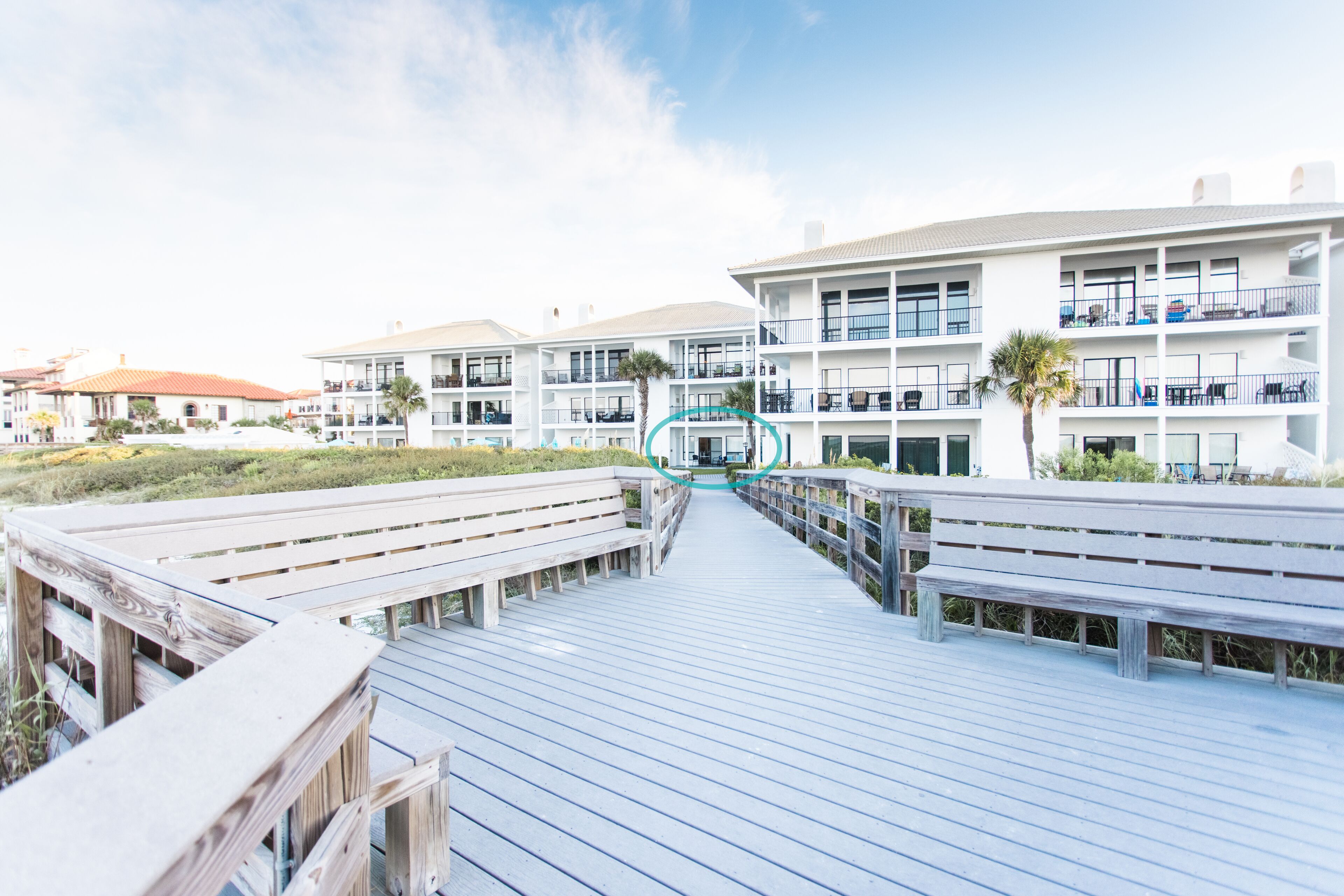 Un muelle de madera que conduce a un hotel de varios pisos con balcones y terraza.