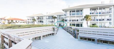 Un muelle de madera que conduce a un hotel de varios pisos con balcones y terraza.