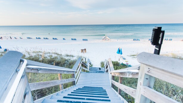 Eine Holztreppe führt zu einem Strand mit freiem Blick auf das Meer und Strandliegen.