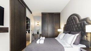 Un dormitorio moderno con una cama grande, un armario de madera oscura y una mesita de noche con una lámpara.