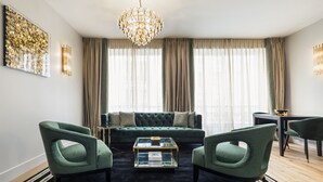Una sala de estar moderna con un sofá verde, dos sillones verdes, una mesa de centro de cristal y una araña.