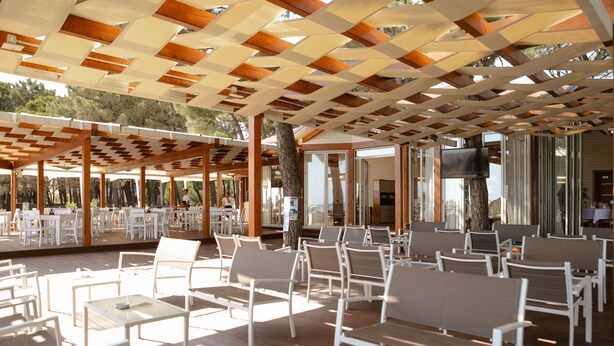 Un espace extérieur aménagé avec des tables et des chaises blanches, un plafond en bois et un grand écran.