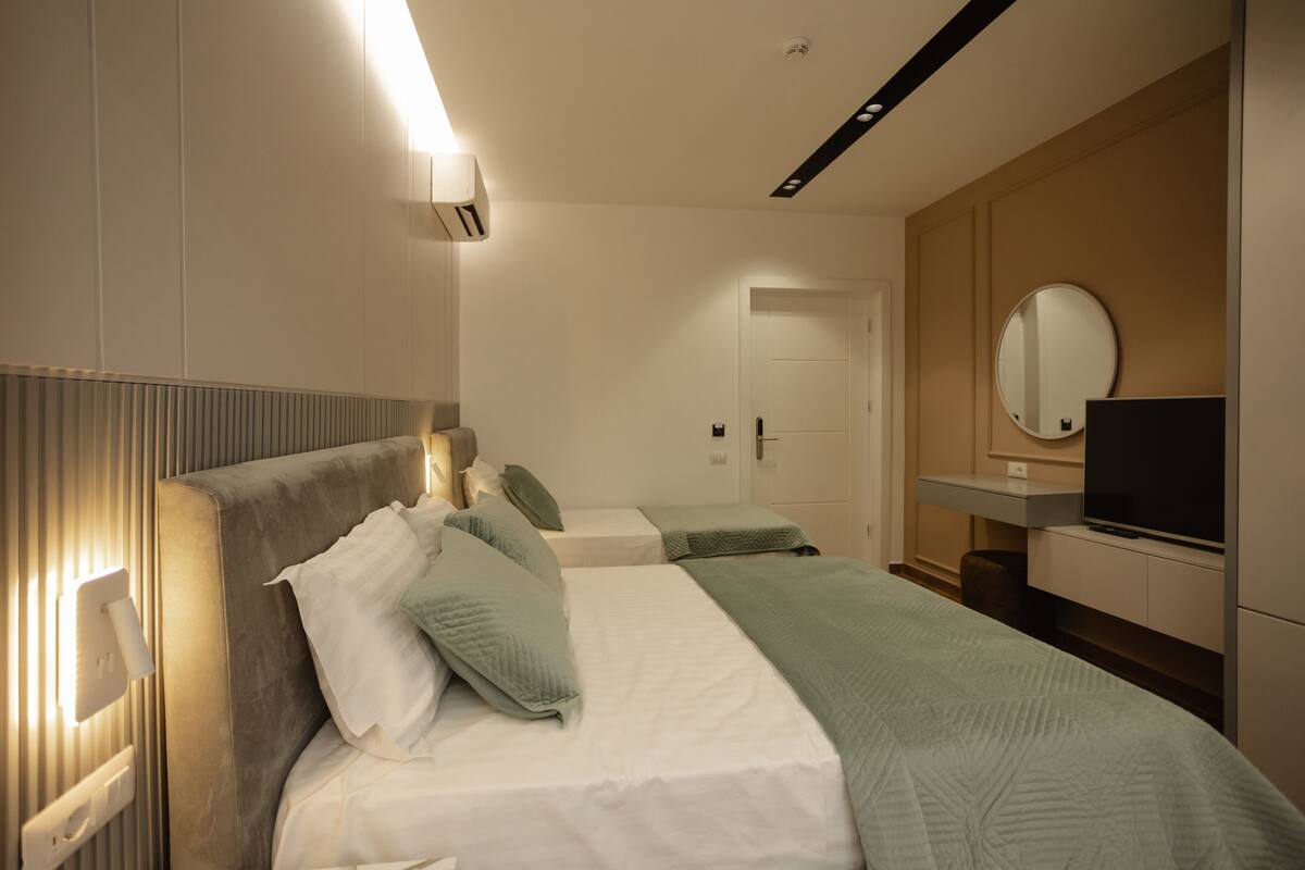 Una habitación de hotel con una cama grande, mesitas de noche, un televisor y un espejo.
