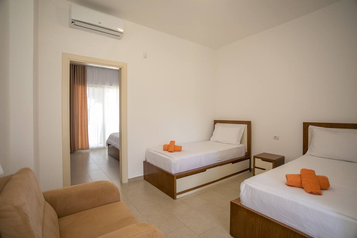 Habitación de hotel con dos camas, un sofá y una mesita de noche pequeña.