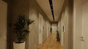 Un long couloir étroit, doté d’un plancher en bois, de murs blancs et de portes des deux côtés. Des plantes en pot sont disposées le long du couloir.