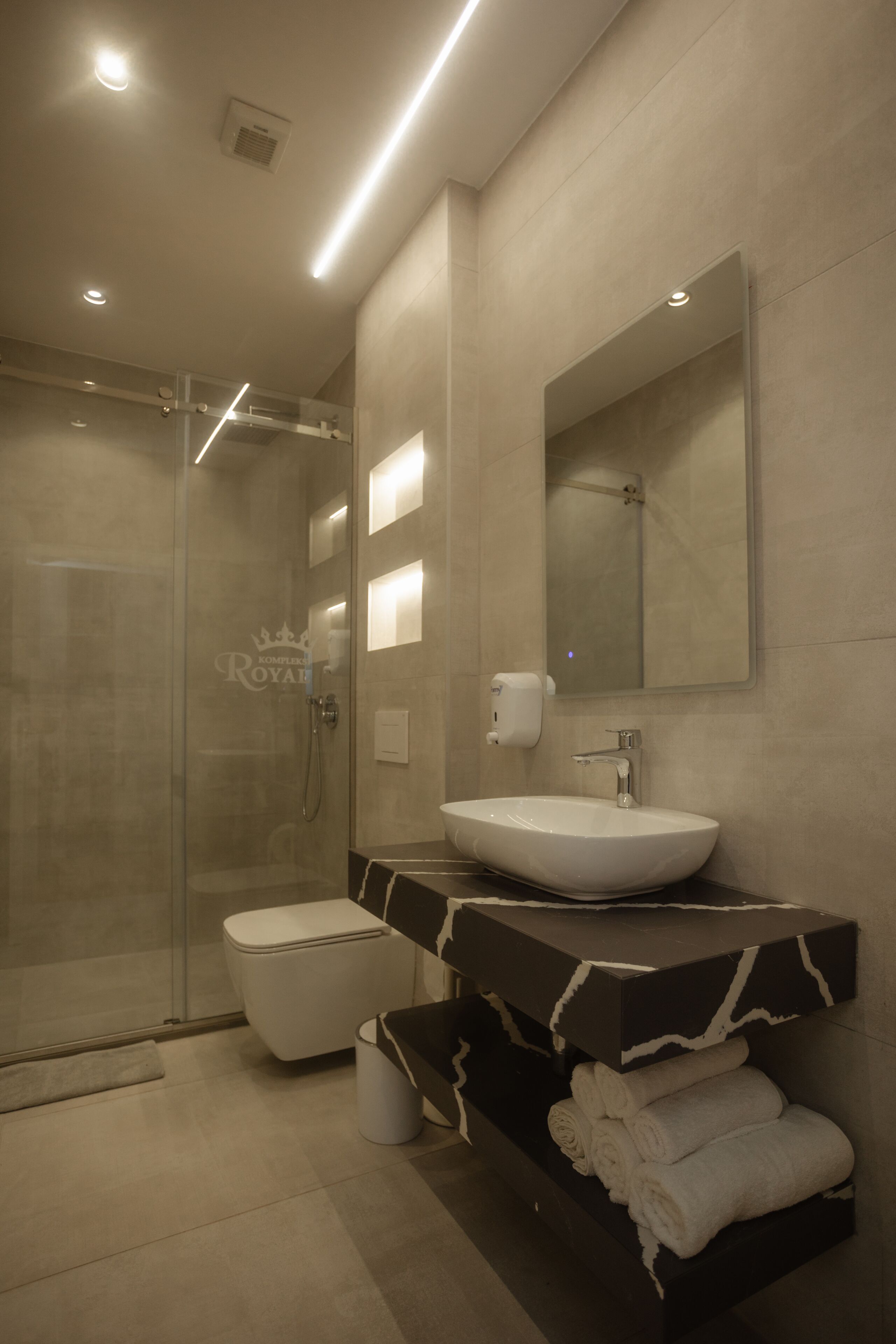 A modern bathroom with a glass shower enclosure, a white sink, and a vanity with marble countertops.