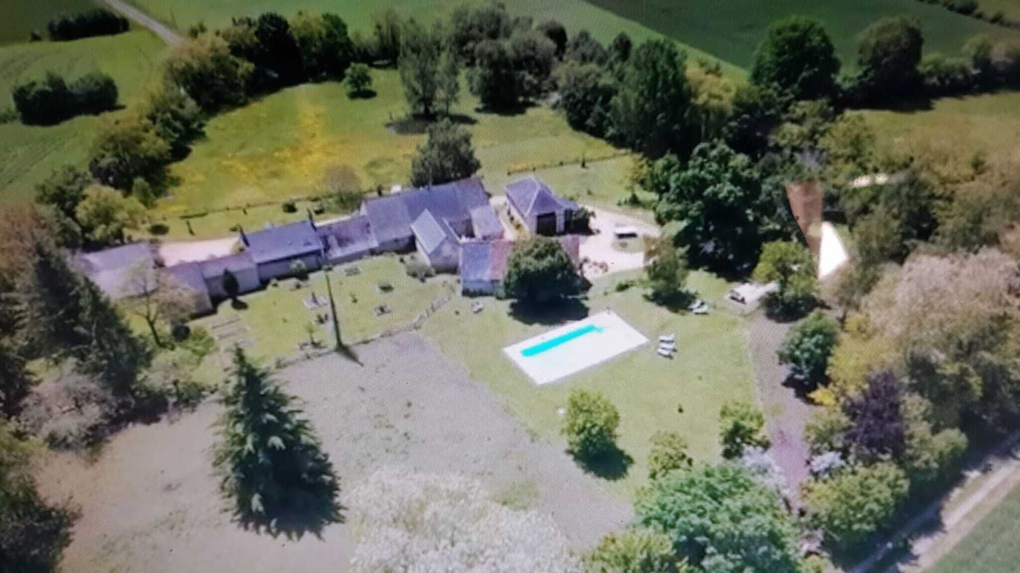 An aerial view of a property with a large house, a swimming pool, and surrounding greenery.
