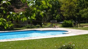 Ein rechteckiger Pool mit Fliesenrand, umgeben von einer Rasenfläche und Bäumen.