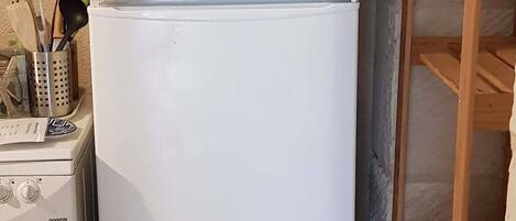 Een witte koelkast met vriesvak bovenin, een kookplaat en een houten plankenunit tegen een structuurwand.