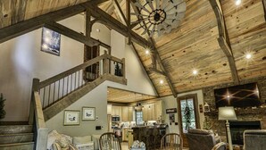 A spacious living area with a wooden staircase, a dining table set with a centerpiece, and a fireplace.