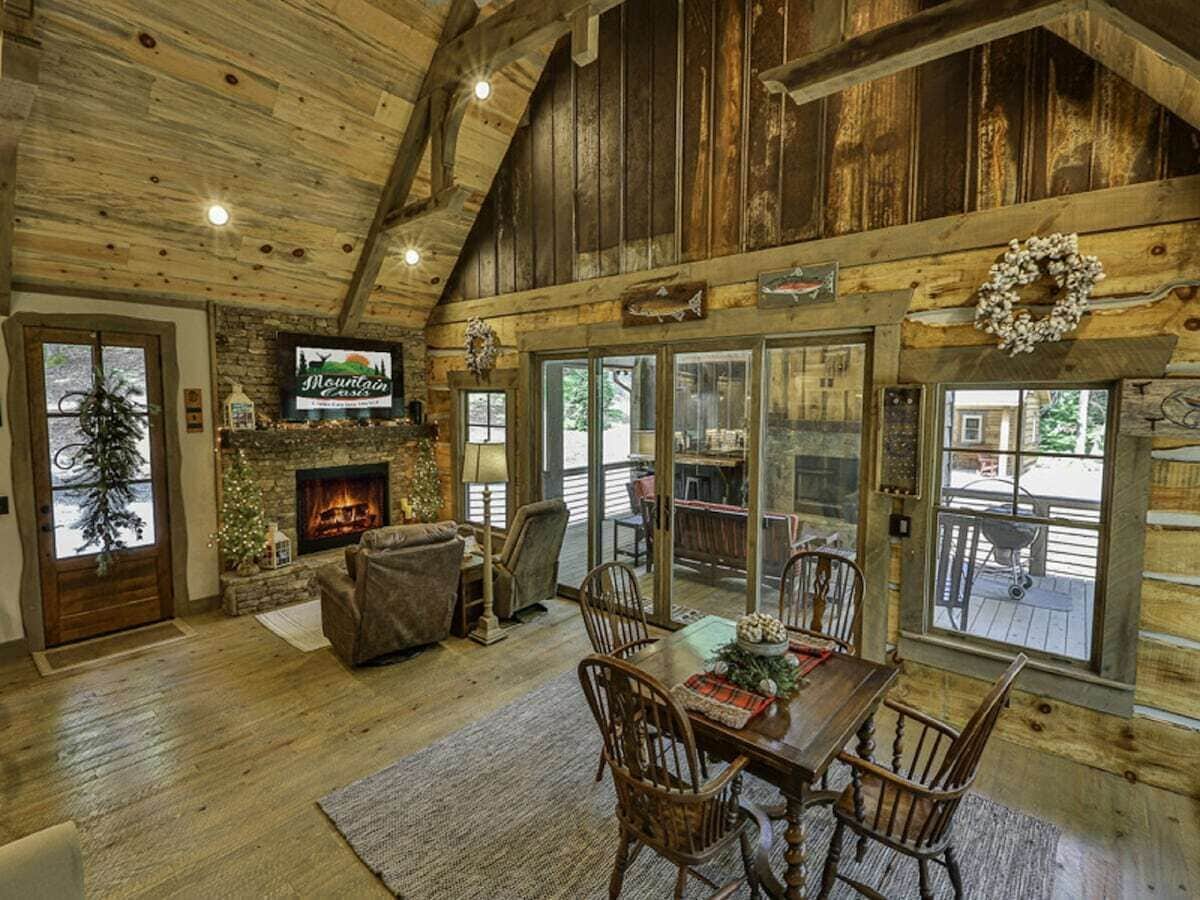 A rustic cabin interior with a fireplace, wooden dining table, and comfortable seating.
