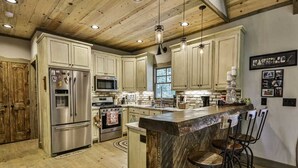 A spacious kitchen with wooden ceiling beams, stainless steel appliances, and a marble island with bar stools.